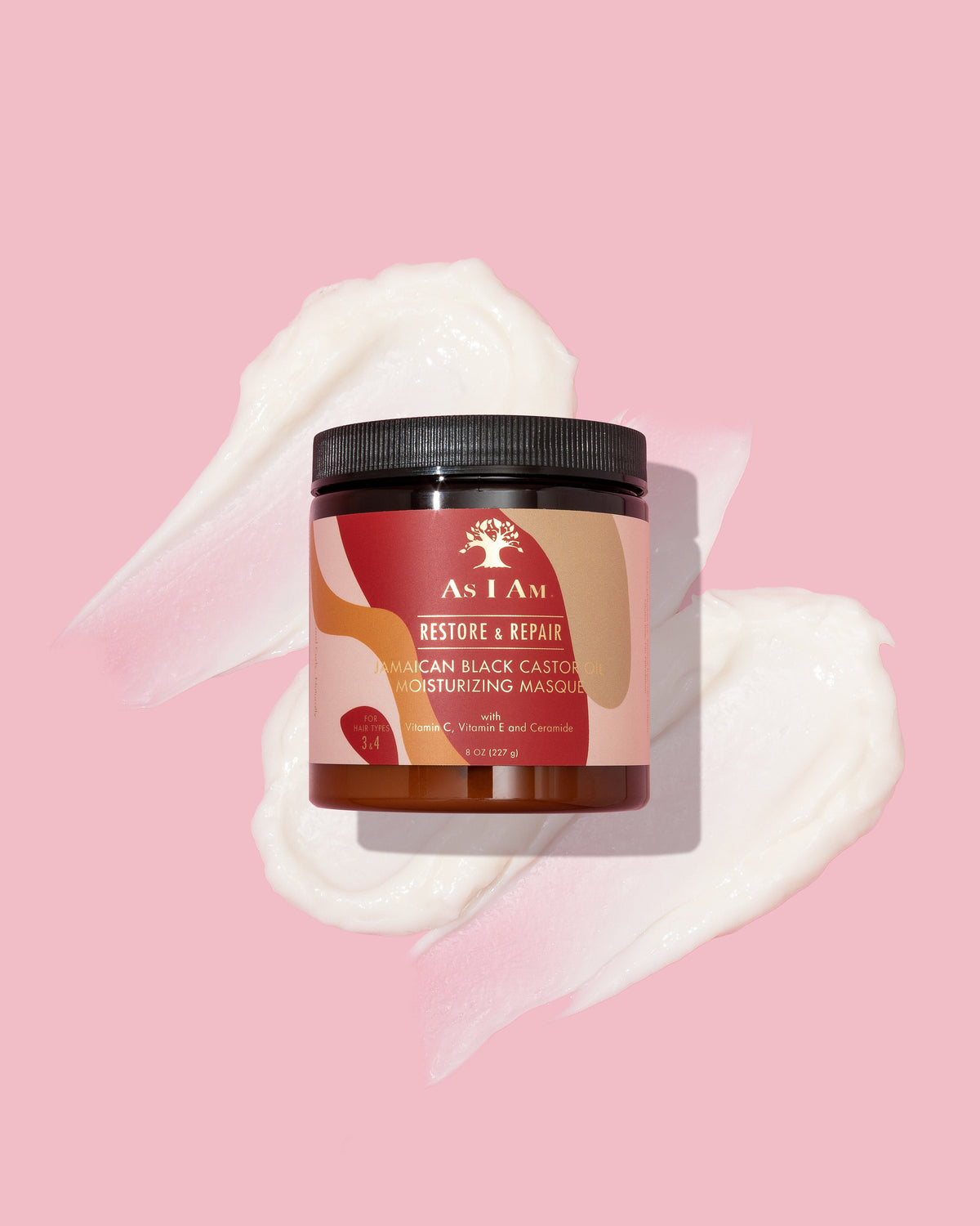 As I Am Jamaican Black Castor Oil Moisturizing Masque (227g) placed on a pink background with three white, creamy blobs of the mask scattered around.