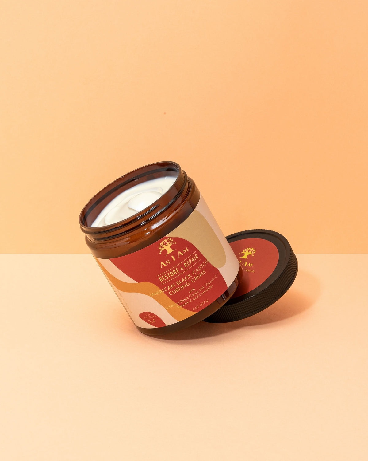 Open plastic can from As I Am Jamaican Black Castor Oil Curling Creme. White cream in brown tin with red label and black lid.