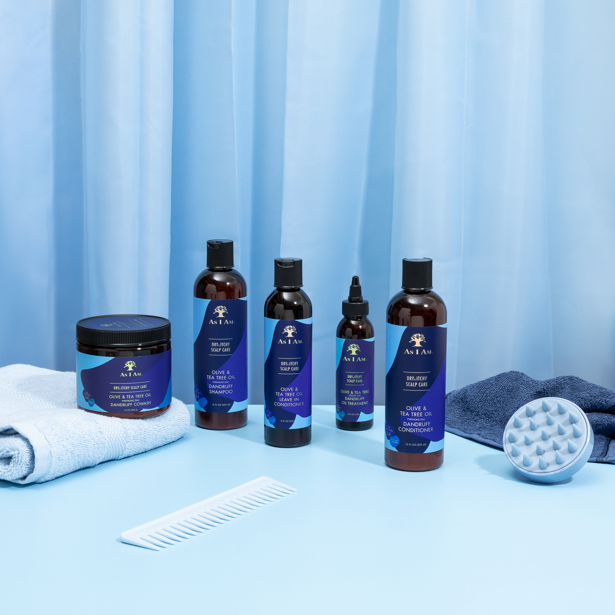 Product image of the As I Am Dry & Itchy Scalp Care range, which includes conditioner, oil treatment and other products, presented with a comb, a massage brush and towels on a light blue background.
