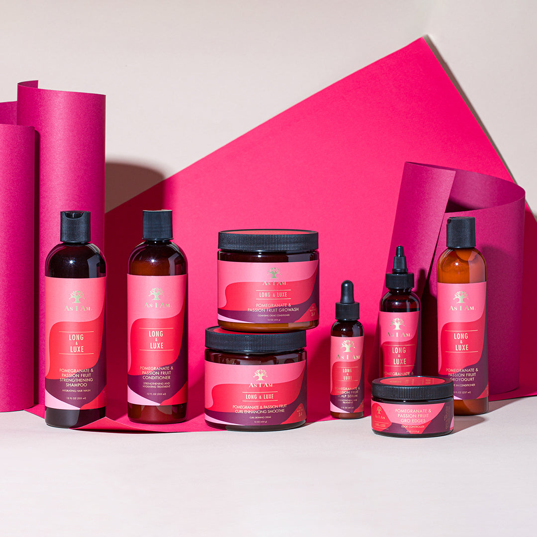 The image shows As I Am Long and Luxe Strengthening Shampoo, Conditioner, GroHair Oil and other products from the series. The products are arranged in front of a pink background.