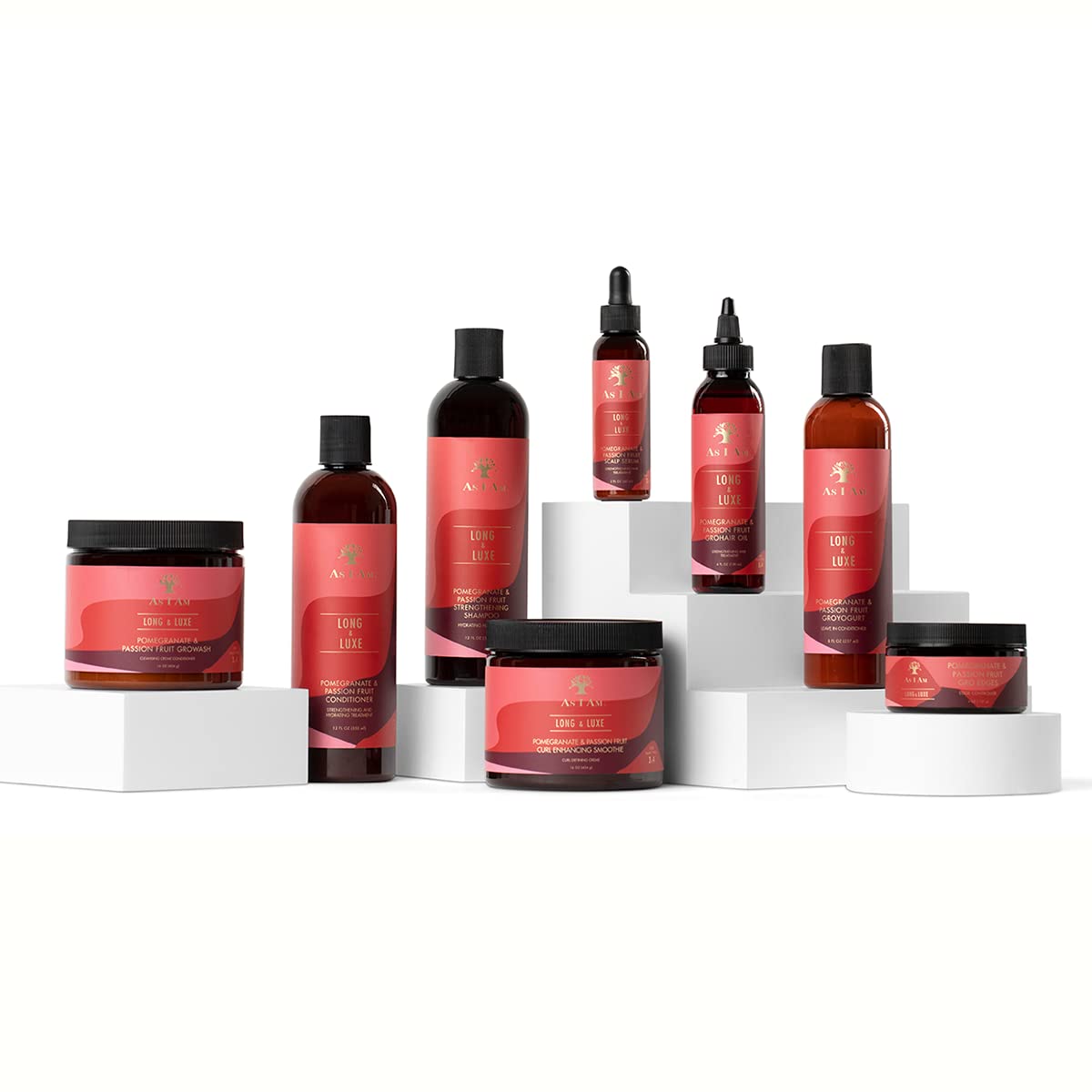 The image shows As I Am Long and Luxe Strengthening Shampoo, Conditioner, GroHair Oil and other products from the range, arranged on white podiums against a white background.
