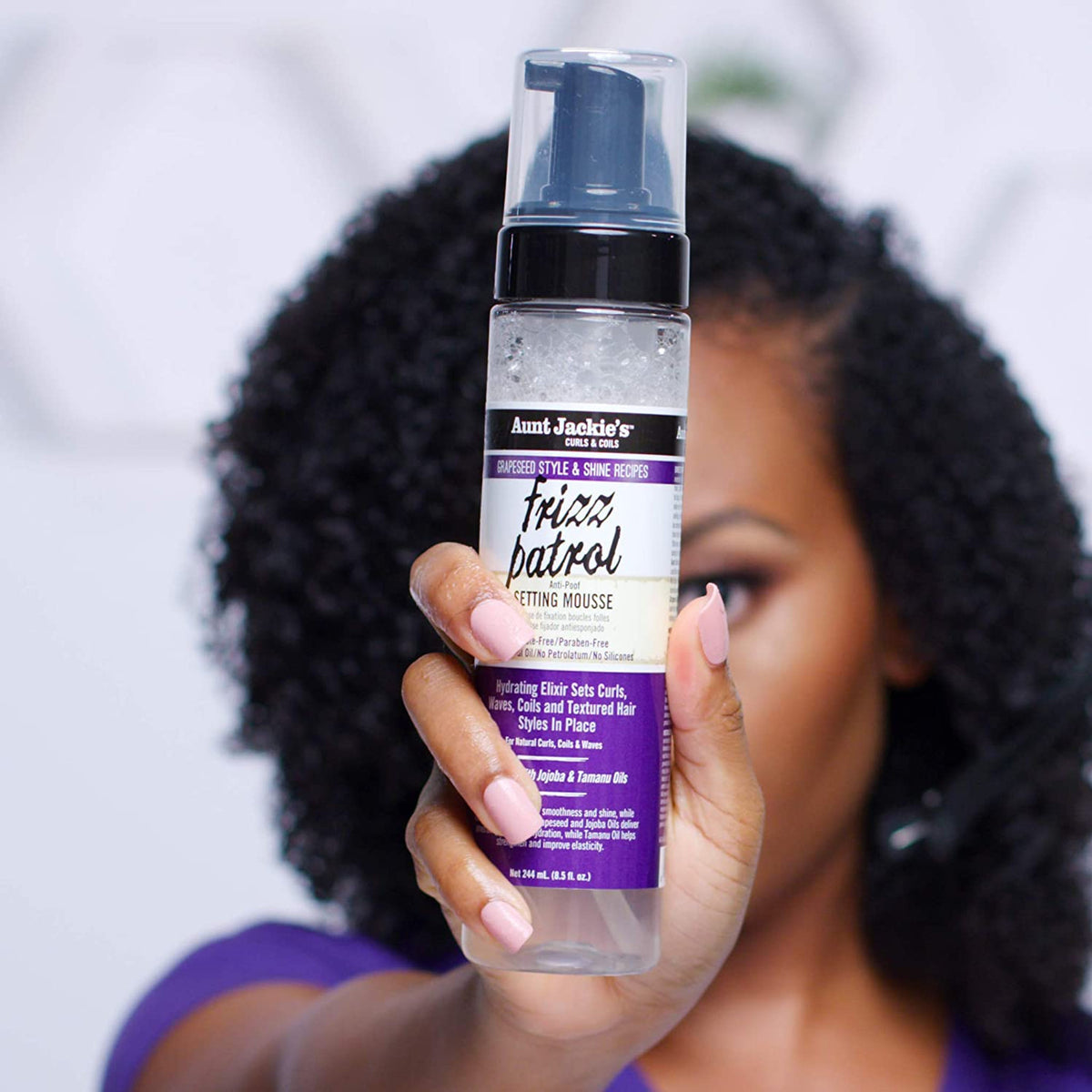 A person with defined curls holds Aunt Jackie's Frizz Patrol Mousse. 
