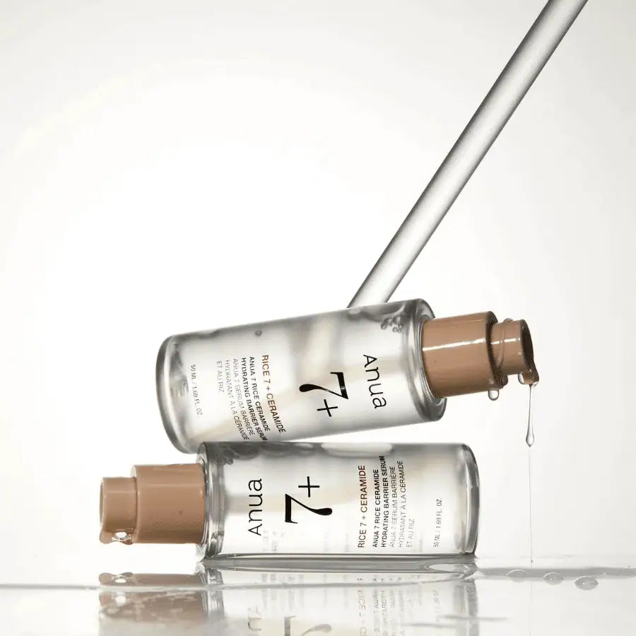Two transparent bottles of Anua Rice 7 Ceramide Hydrating Barrier Serum 50ml, where the serum drips from the pump.