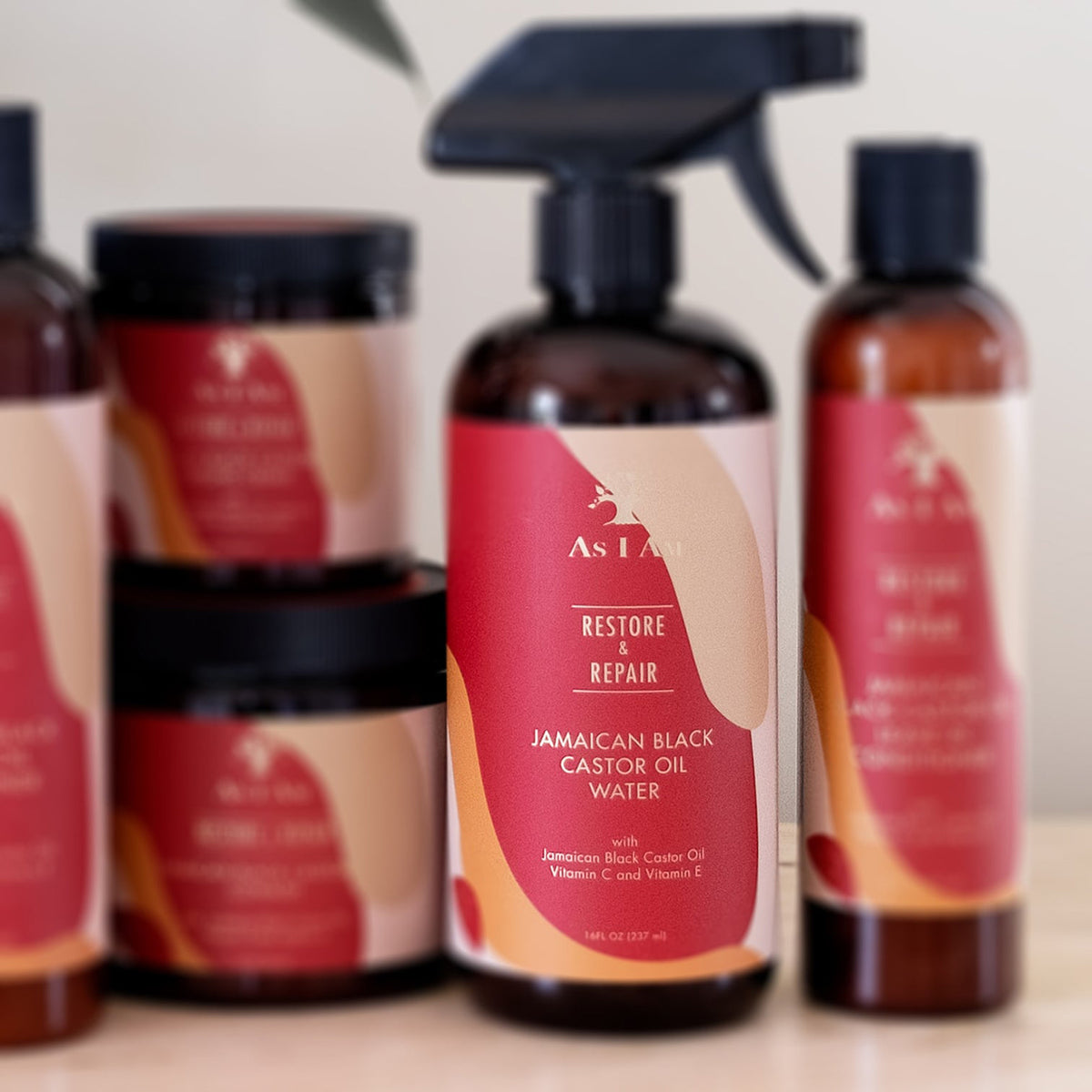 As I Am Jamaican Black Castor Oil Water (473 ml) spray bottle in the foreground, surrounded by other As I Am hair care products on a shelf.