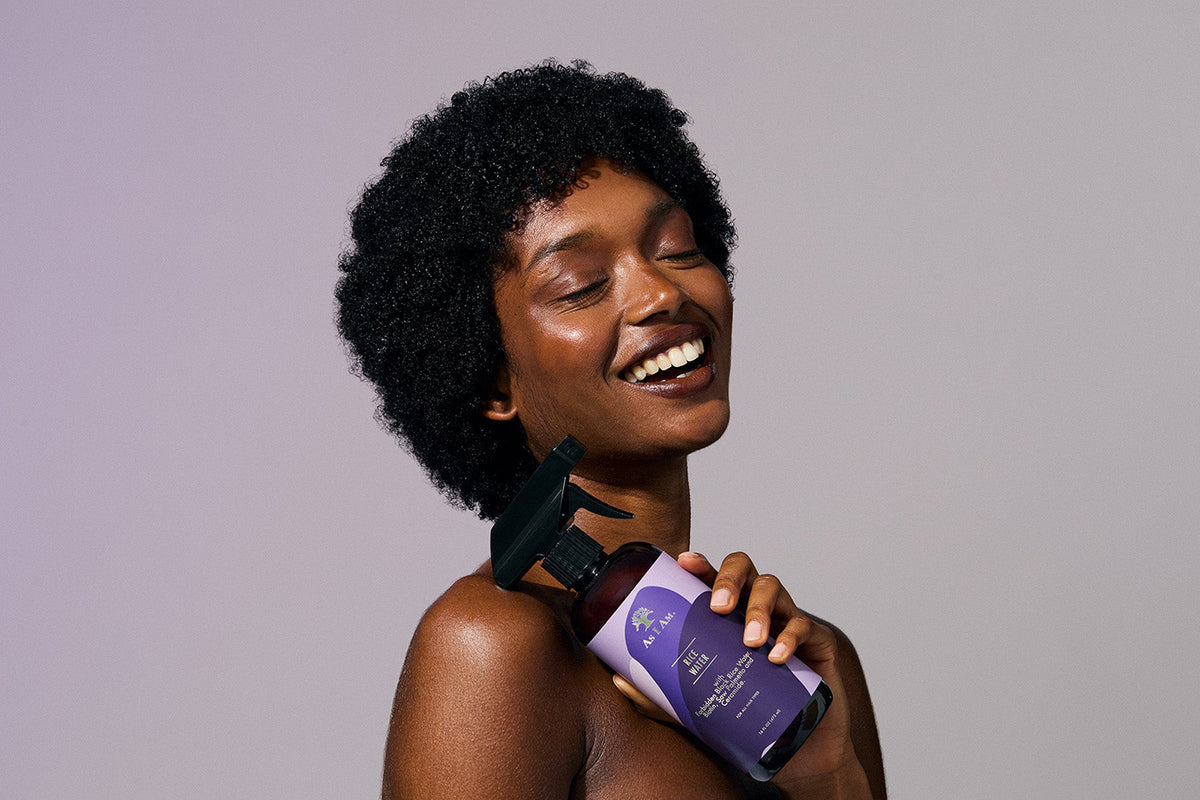 A woman holds a bottle of As I Am Rice Water Spray.