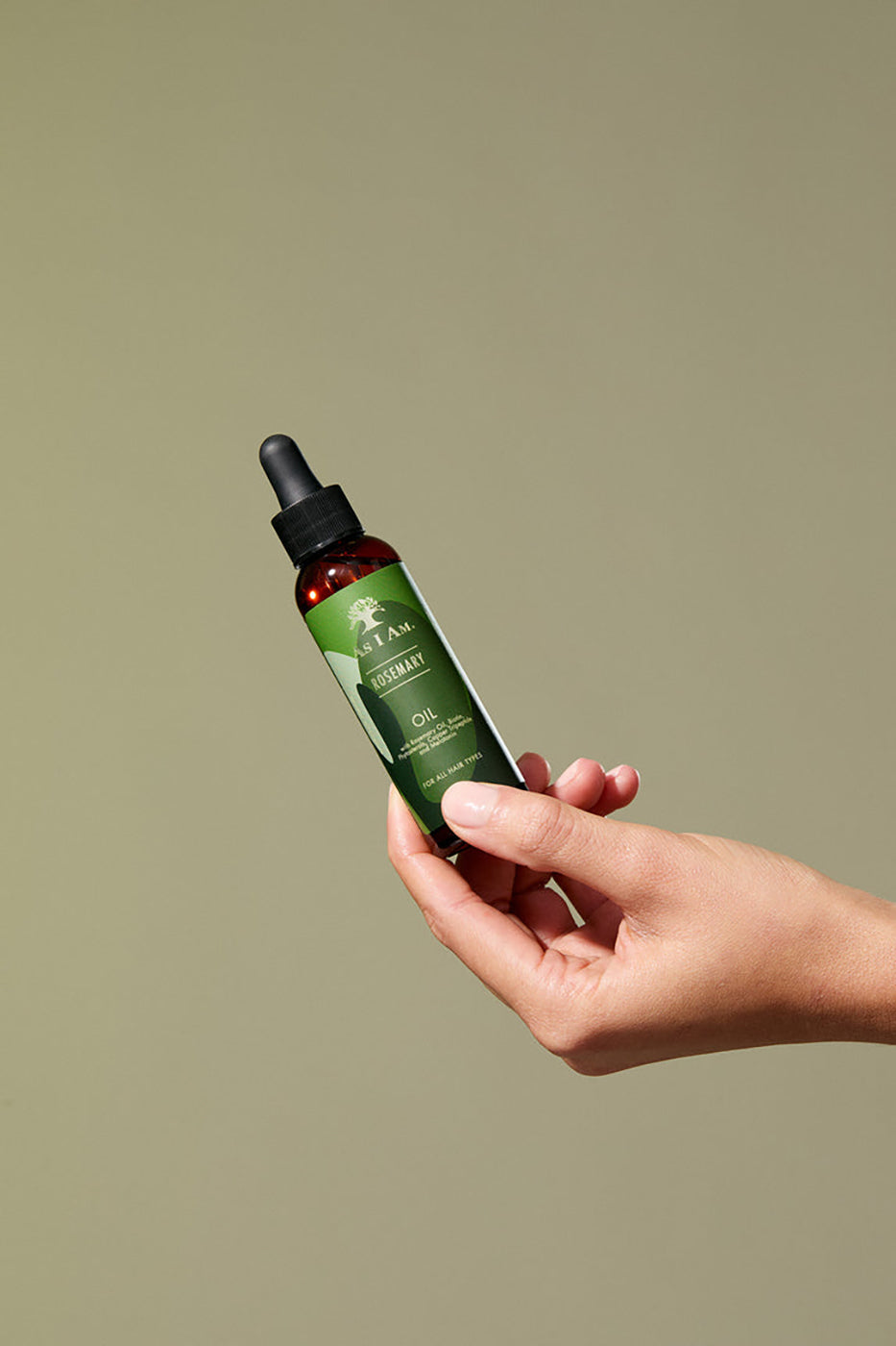 A hand holds a bottle of As I Am Rosemary Oil (60ml) in front of a light background.