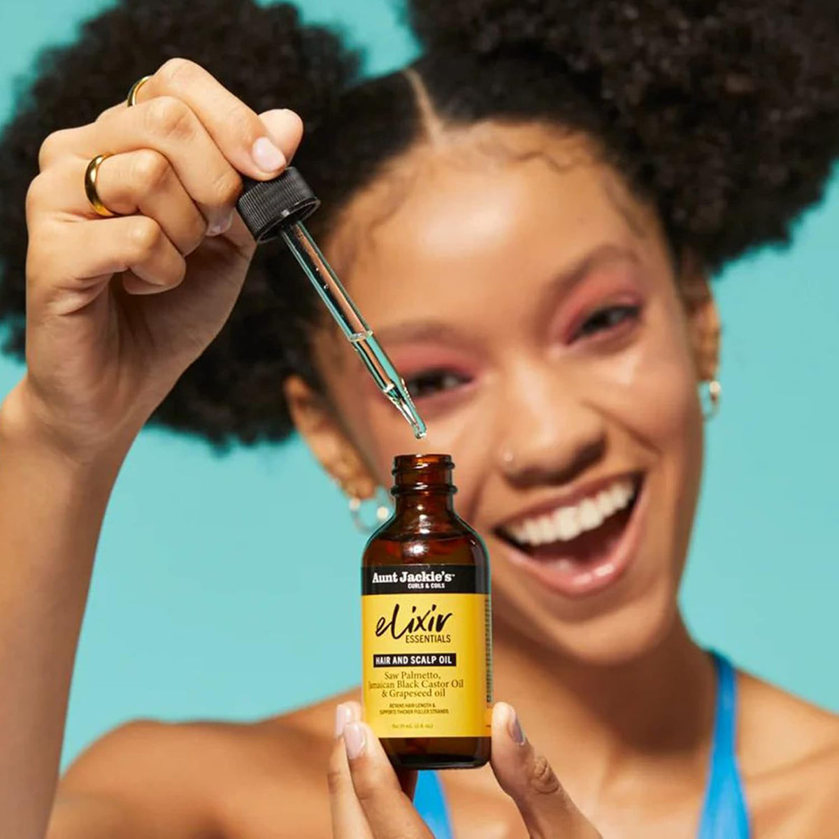 Close-up of a hand dripping Aunt Jackie's Elixir Essentials Hair and Scalp Oil from a dropper into a brown glass bottle.