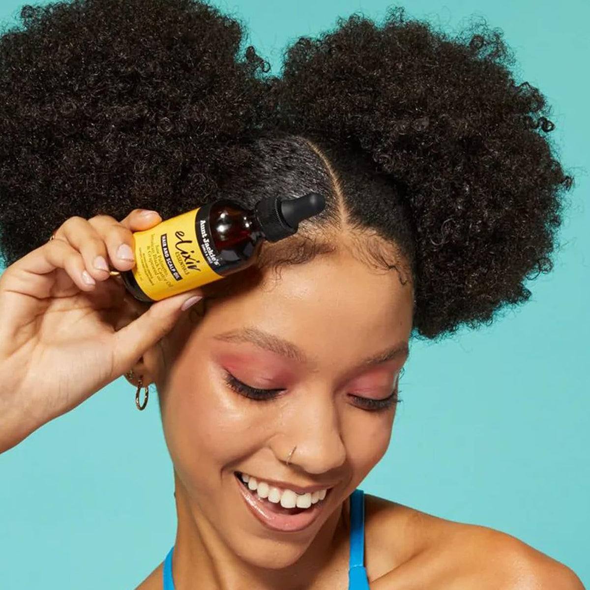 Hand holding Aunt Jackie's Elixir Essentials Hair and Scalp Oil against the scalp of a person with thick, curly hair.