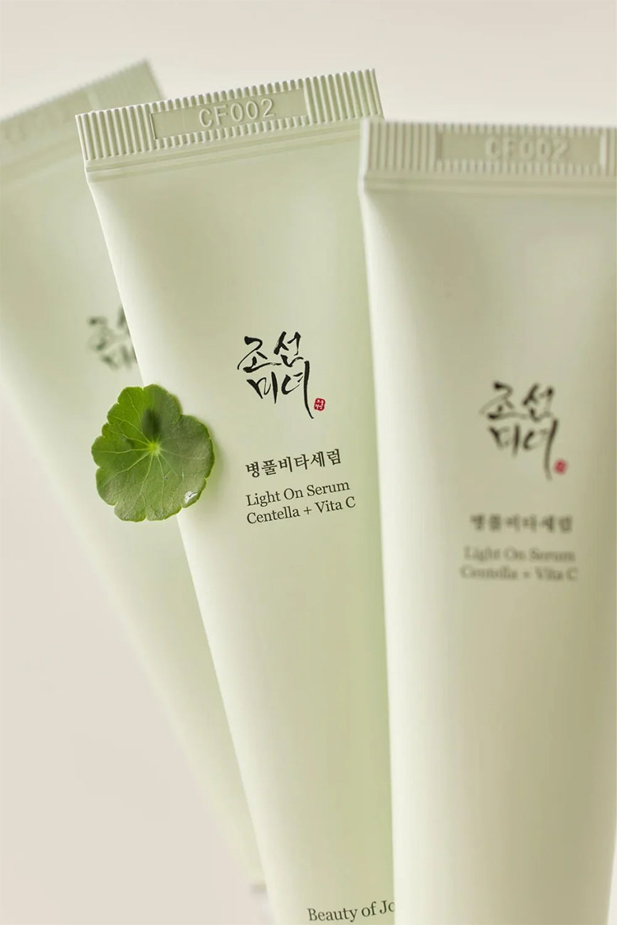 Several tubes of Beauty of Joseon Light On Serum Centella + Vita C 30ml with centella leaf in focus on a beige background.