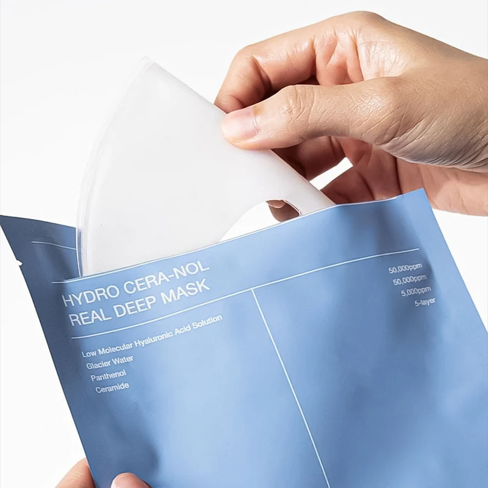 Hand takes Biodance Hydro Cera-nol Real Deep Mask out of blue packaging with visible white sheet mask.