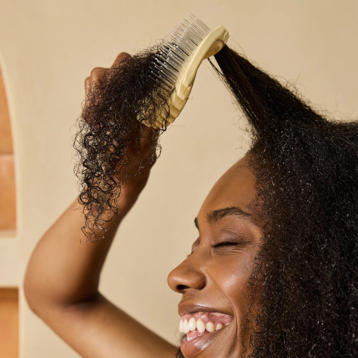 Woman combs wet, curly hair with yellow detangling comb to untangle knots after washing hair.