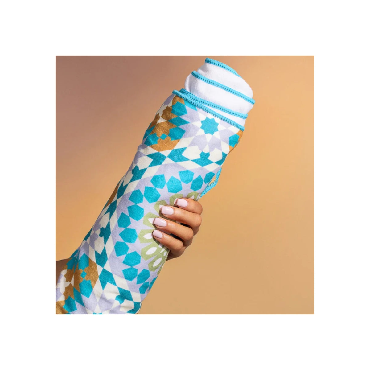 Hand holding colorful Bounce Curl Micro-fiber Towel with blue and green patterns against beige background.