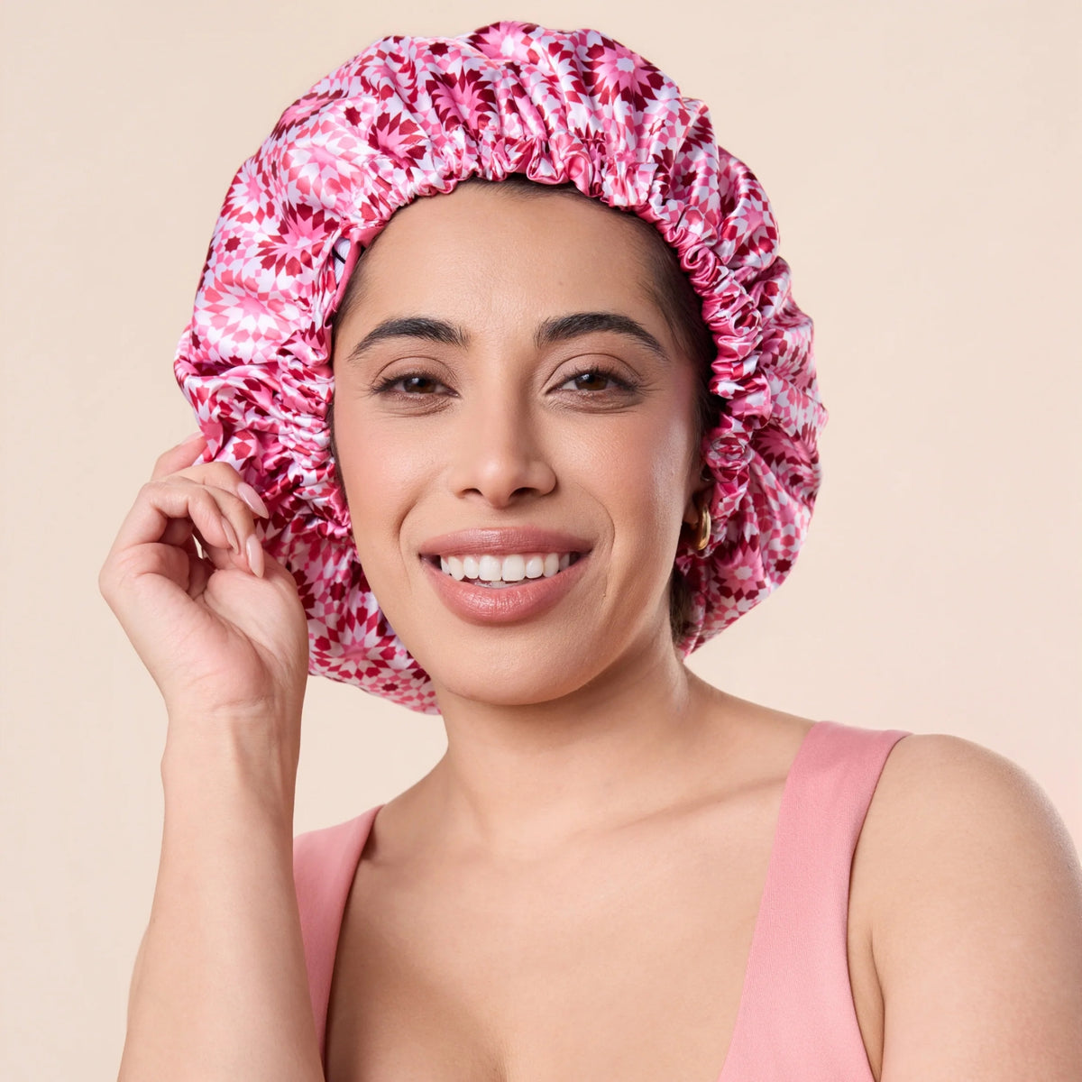 Smiling woman with pink patterned satin bonnet for hair care, wearing pink top.