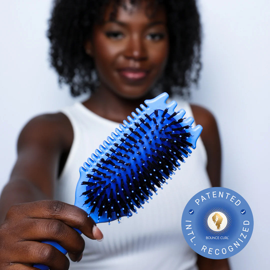 Woman with curly hair holds Bounce Curl Volume EdgeLift Brush Blue with blue and black bristles in focus.