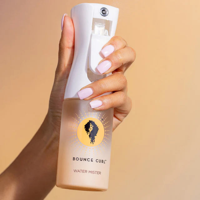 Hand held Bounce Curl Water Mister with white spray nozzle and logo in front of beige background.