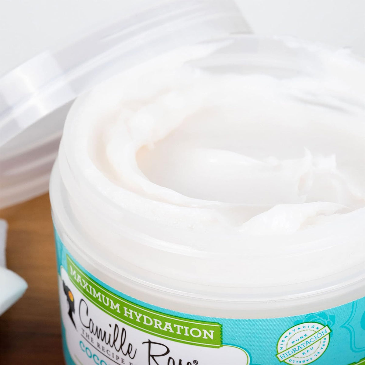 Close-up of the white, creamy consistency of Camille Rose Coconut Water Penetrating Hair Treatment in an open container.