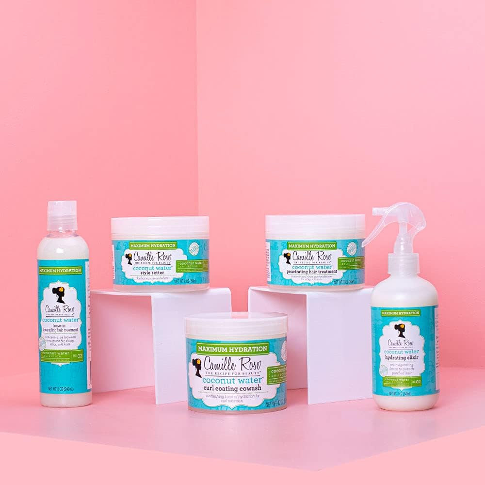 Camille Rose Coconut Water Penetrating Hair Treatment, Curl Coating Cowash and other products on white podiums against pink background.