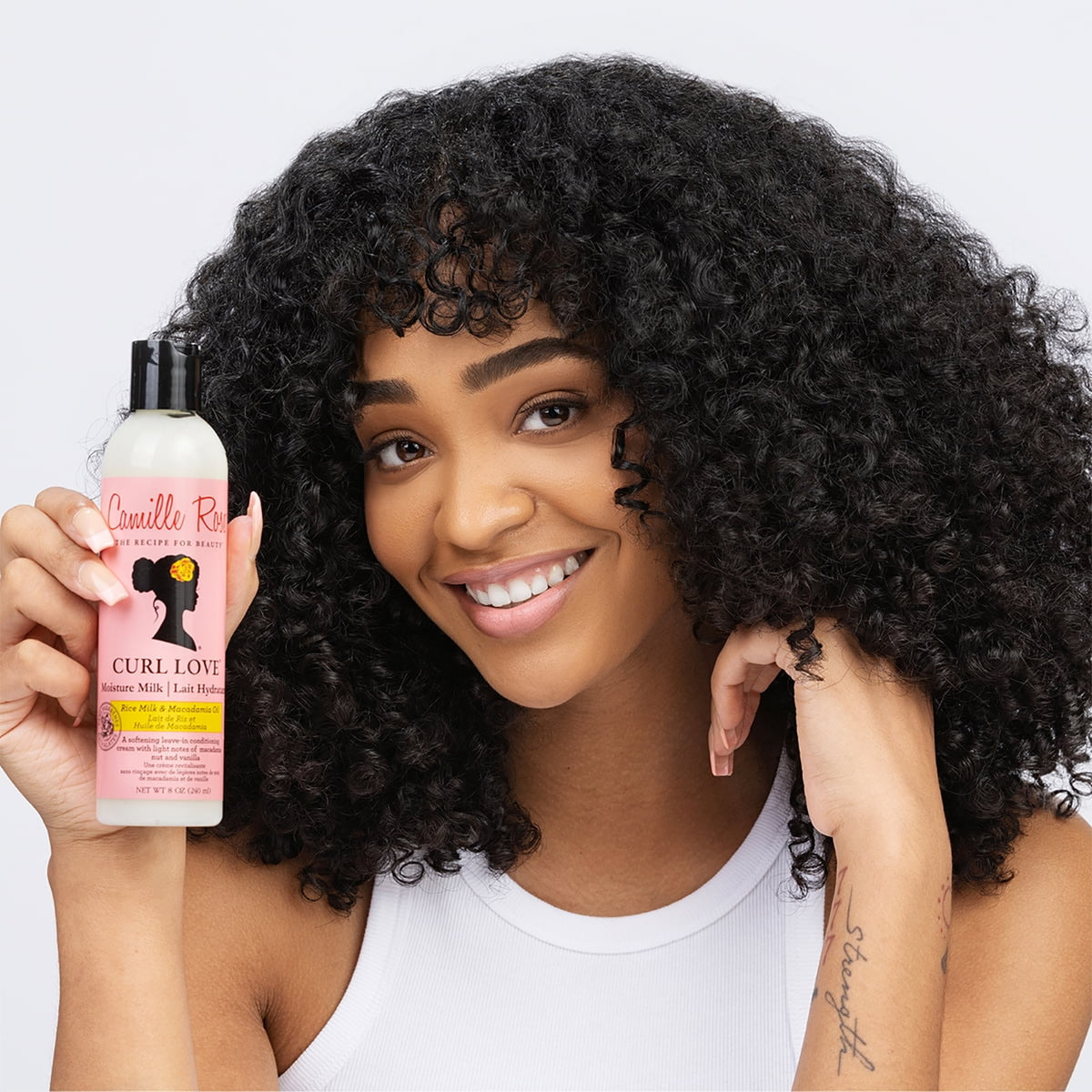 Camille Rose Curl Love Moisture Milk in white bottle with black cap is held by a woman with curly hair.