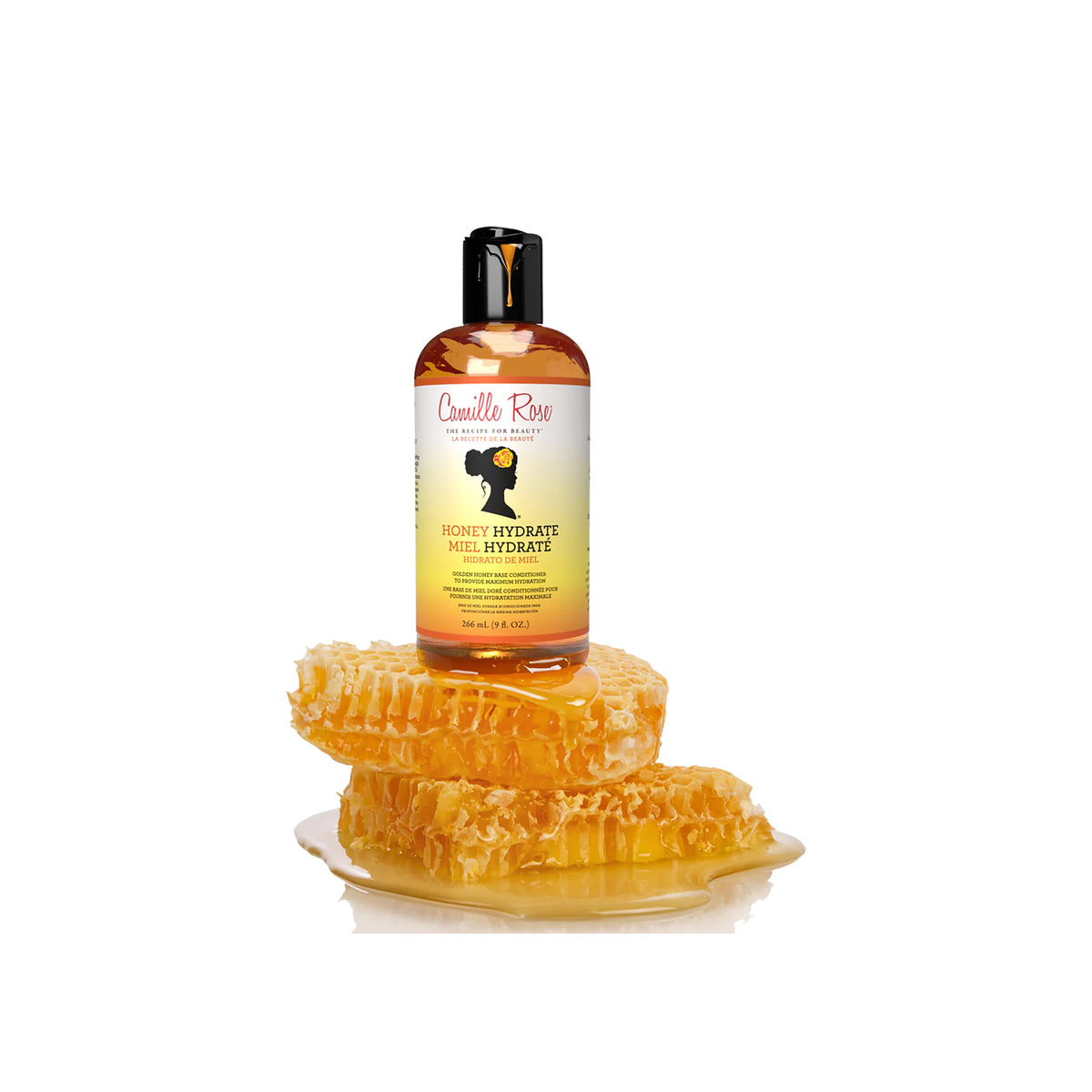 Golden bottle of Camille Rose Honey Hydrate Leave-In Conditioner on a white background, surrounded by gingerbread.