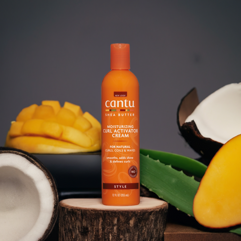 Close-up of an orange bottle of Cantu Shea Butter Curl Activator. The bottle stands in front of tropical fruits that symbolize the product's natural ingredients.