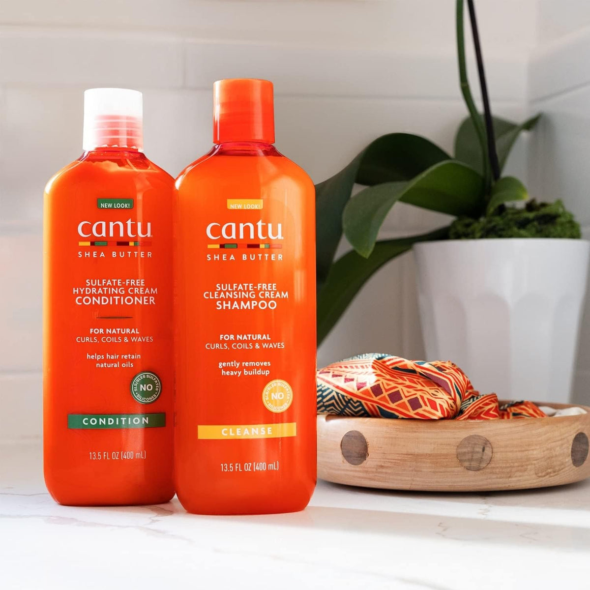 Two orange bottles: Cantu Shea Butter Hydrating Cream Conditioner and Cleansing Cream Shampoo.