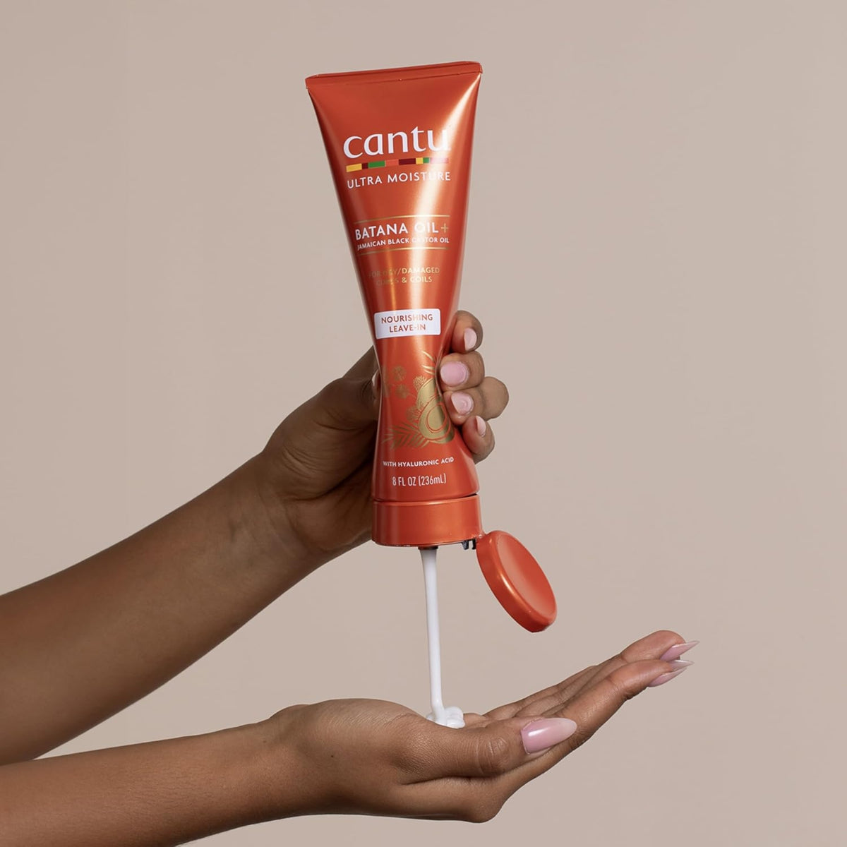 Hand squeezes Cantu Ultra Moisture Batana Oil+ nourishing leave-in cream into the palm of another hand.