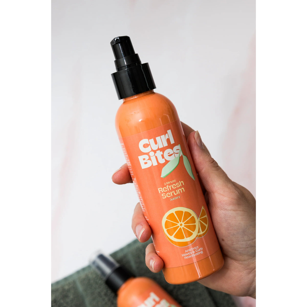 Hand holds Curl Bites 2 Minute Refresh Serum, orange bottle with pump and orange motif.