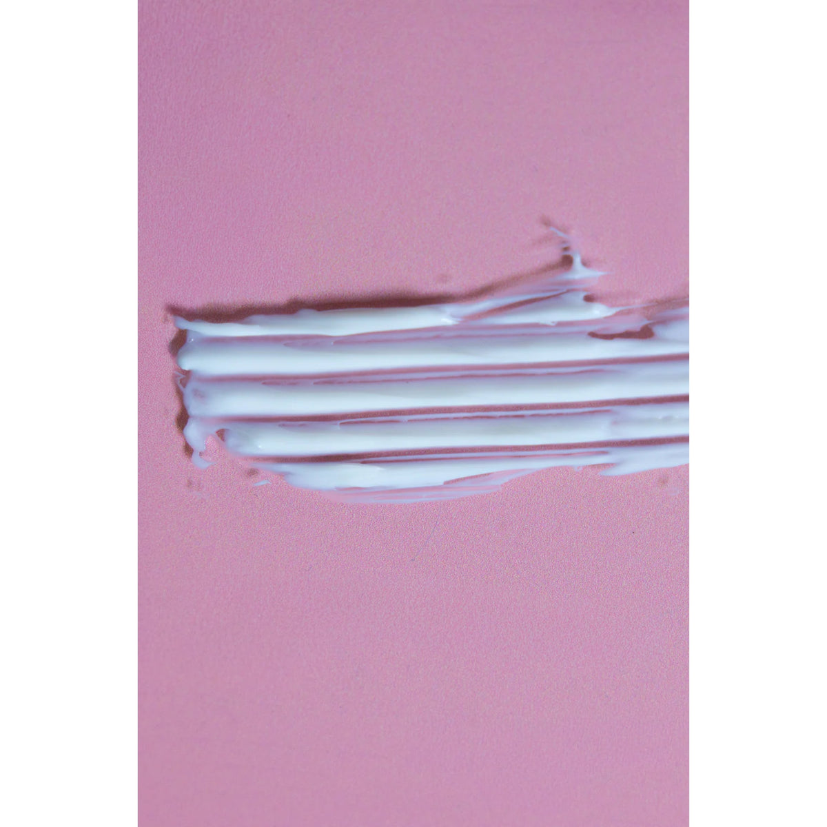 White creamy lotion smeared in stripes with comb lines on a pink background.