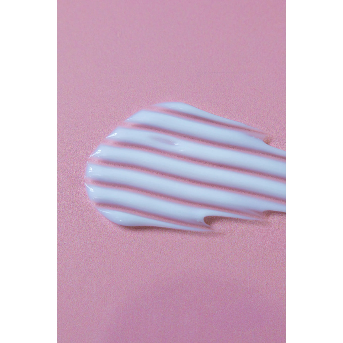 Creamy white skin care cream with wavy texture smeared on pink background.