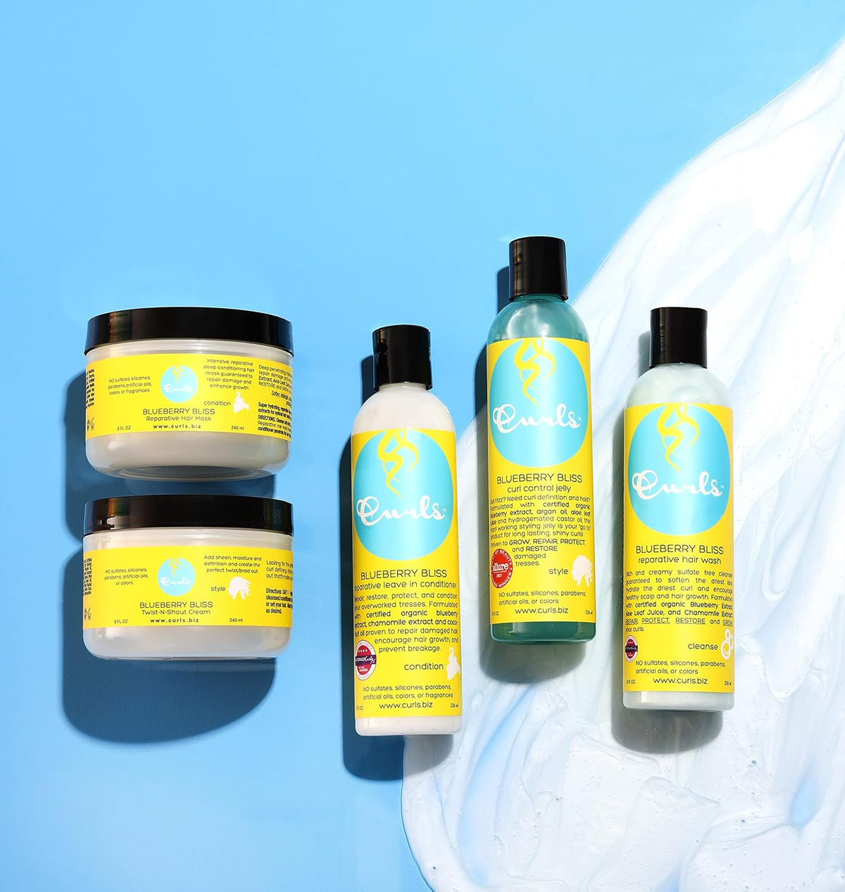 Four Curls Blueberry Bliss products: Two jars of jelly/paste, a bottle of oil and a bottle of leave-in conditioner on a light blue background.