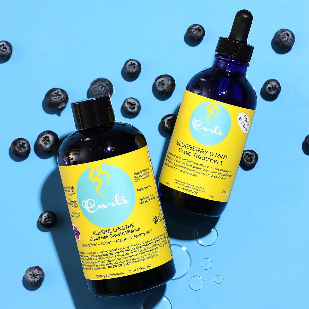 Two Curls products, a scalp treatment and a liquid hair growth vitamin, surrounded by fresh blueberries on a blue background.