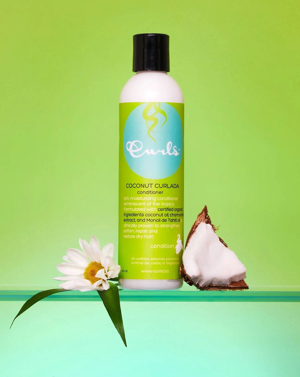 Curls Coconut Curlada Conditioner (240 ml) presented with a coconut and a white flower on a green background. White bottle with green label and black cap. Conditioner with coconut for curly hair.