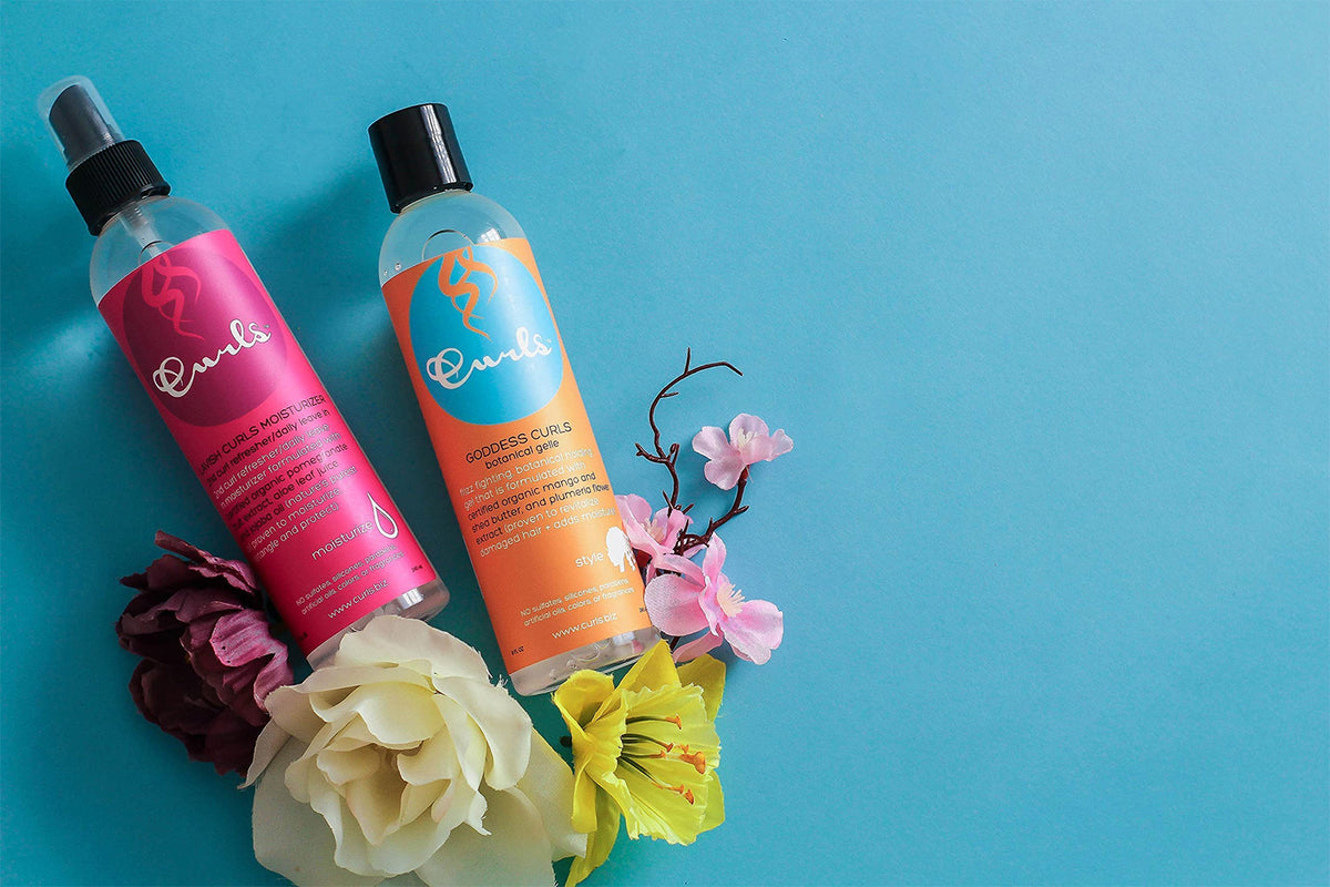 Curls Lavish Curls Moisturizer (pink) and Goddess Curls Botanical Gel (orange) on a blue background with flowers. Hair care products for curls.