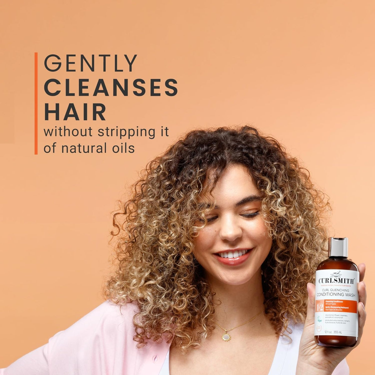 Woman with curly hair smiles and holds Curlsmith Curl Quenching Conditioning Wash, which gently cleanses hair without stripping natural oils.