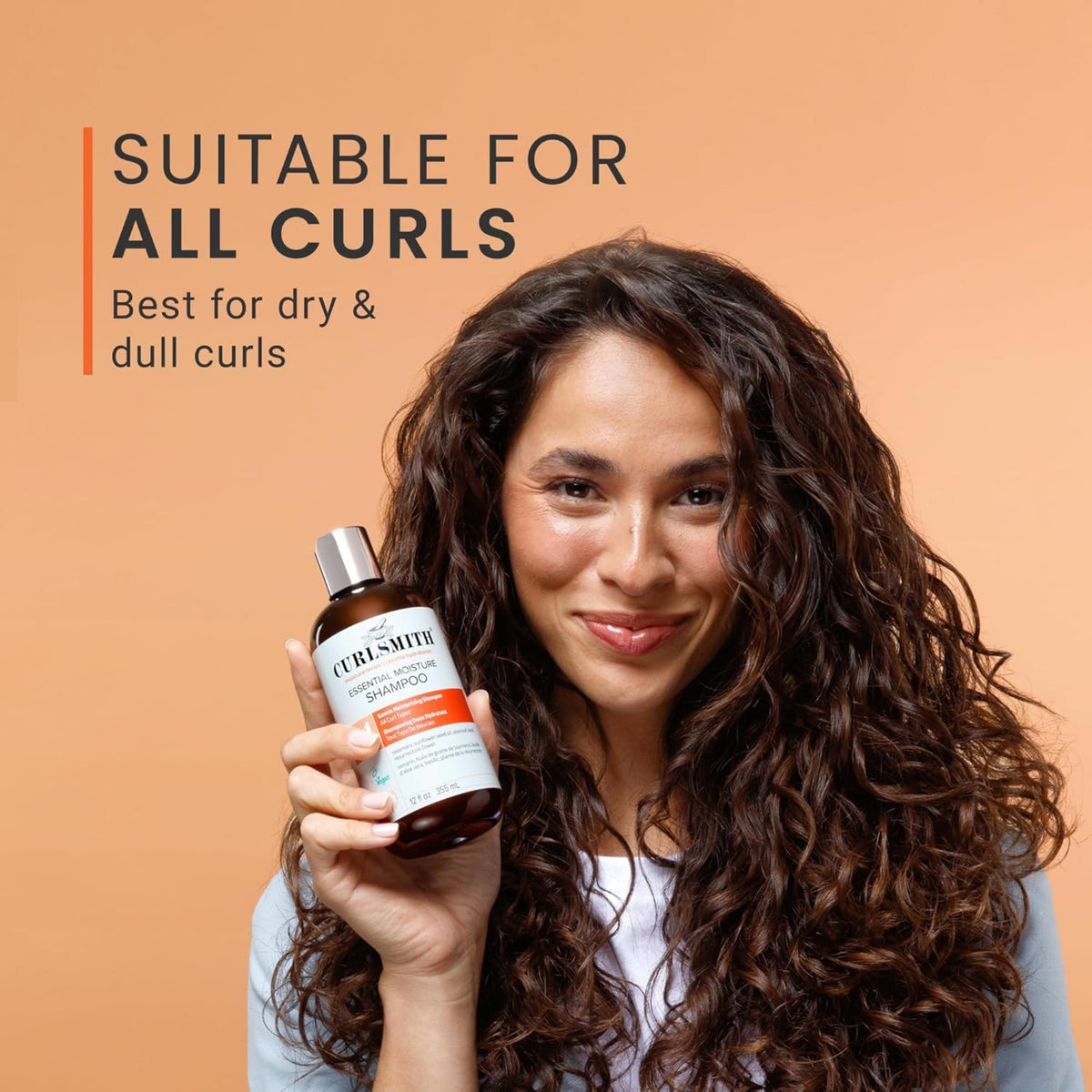 Woman with curly hair holds Curlsmith Essential Moisture Shampoo, suitable for all curls, best for dry and dull hair.