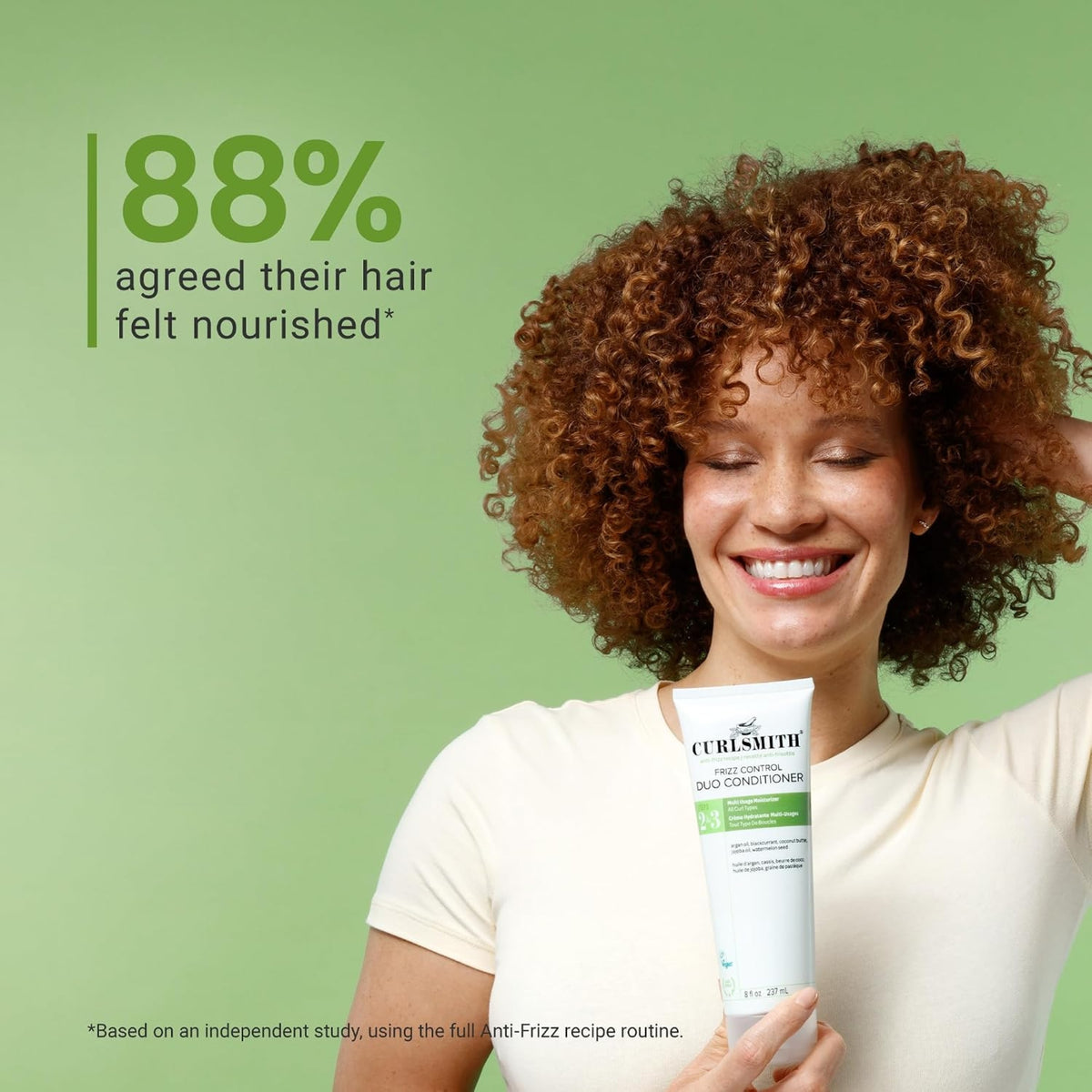 Woman with curly auburn hair smiles and holds Curlsmith Frizz Control Duo Conditioner, 88% experienced nourished hair.