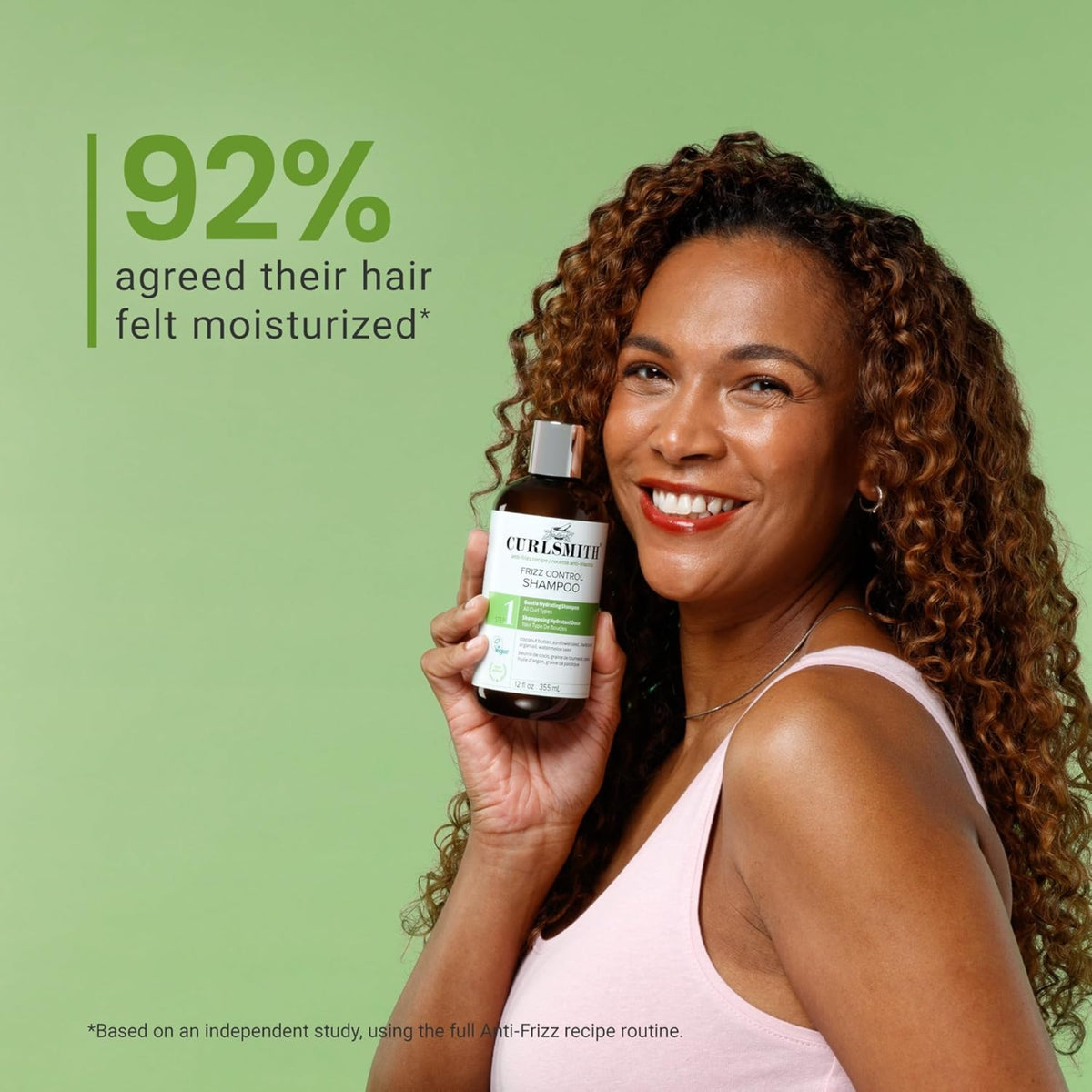 Woman with curly hair smiles and holds Curlsmith Frizz Control Shampoo, 92% experienced more moist hair.