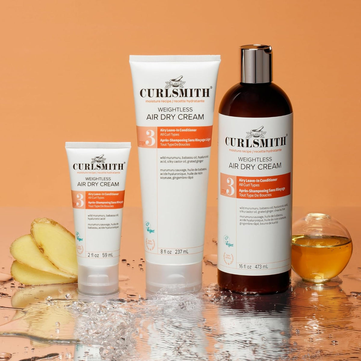 Curlsmith Weightless Air Dry Cream in three sizes with ginger and oil on water reflective surface, orange background.