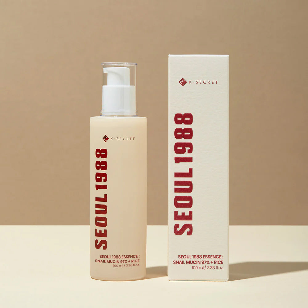 Bottle and box of K-Secret Essence: Snail Mucin 97% + Rice 100 ml standing against beige background.