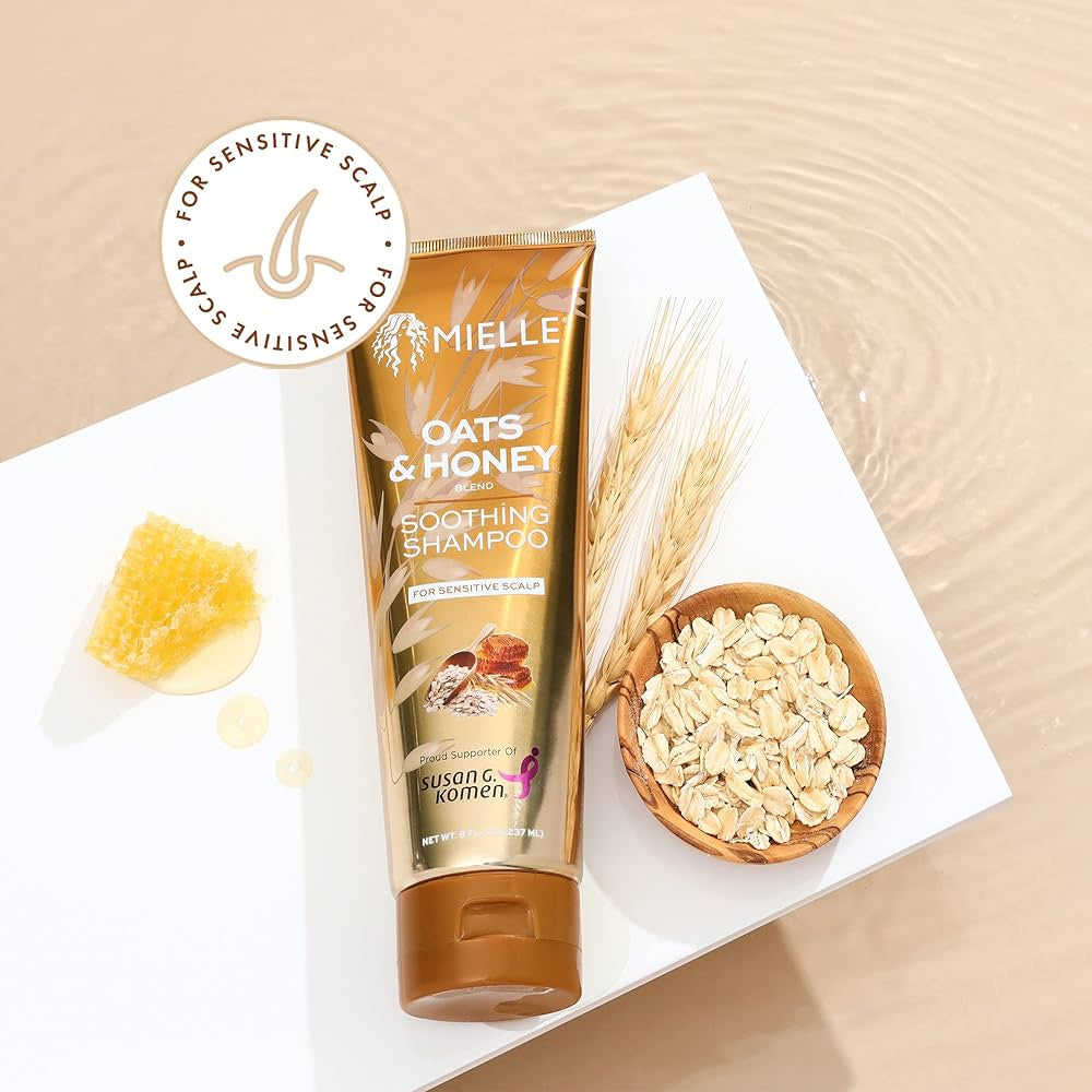 Mielle Oats & Honey Soothing Shampoo 237ml placed on white surface with oats, honey and wheat straw next to it.