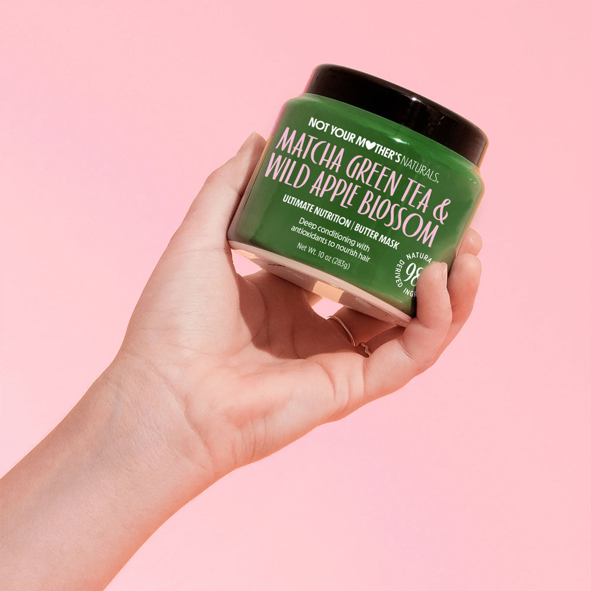Not Your Mother's Matcha Green Tea & Wild Apple Blossom Butter Masque 283g held in hand in front of pink background.