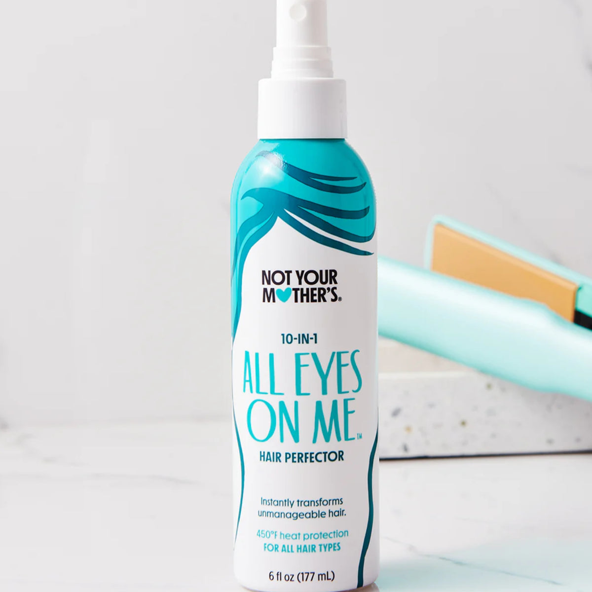 Not Your Mother's All Eyes On Me 10-in-1 hair perfector spray in white bottle with turquoise hair design next to mint green straightener.
