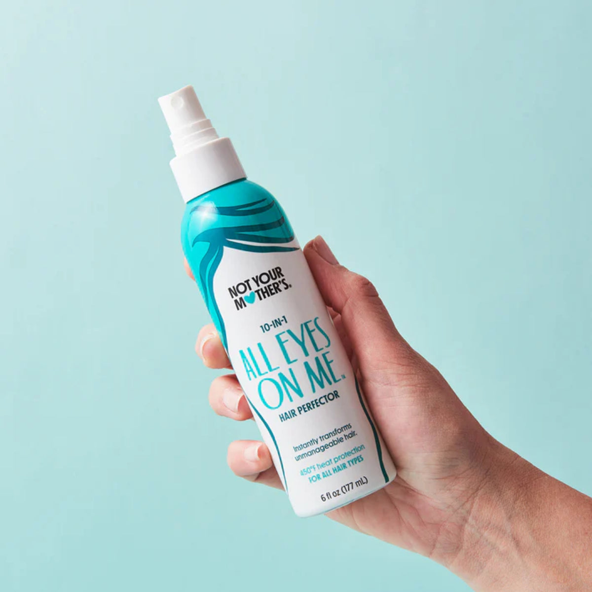 Hand holding Not Your Mother's All Eyes On Me 10-in-1 hair perfector spray against light blue background.