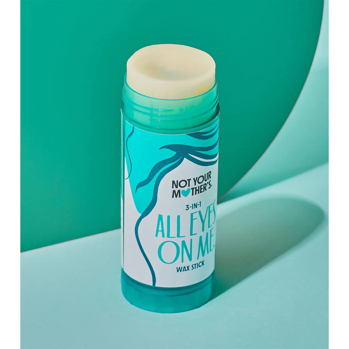 Not Your Mother's All Eyes On Me 3-in-1 wax stick in turquoise tube on green background.