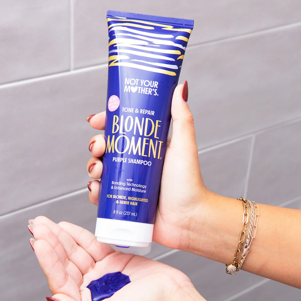 Not Your Mother's Blonde Moment purple purple shampoo held in hand with purple product in palm.