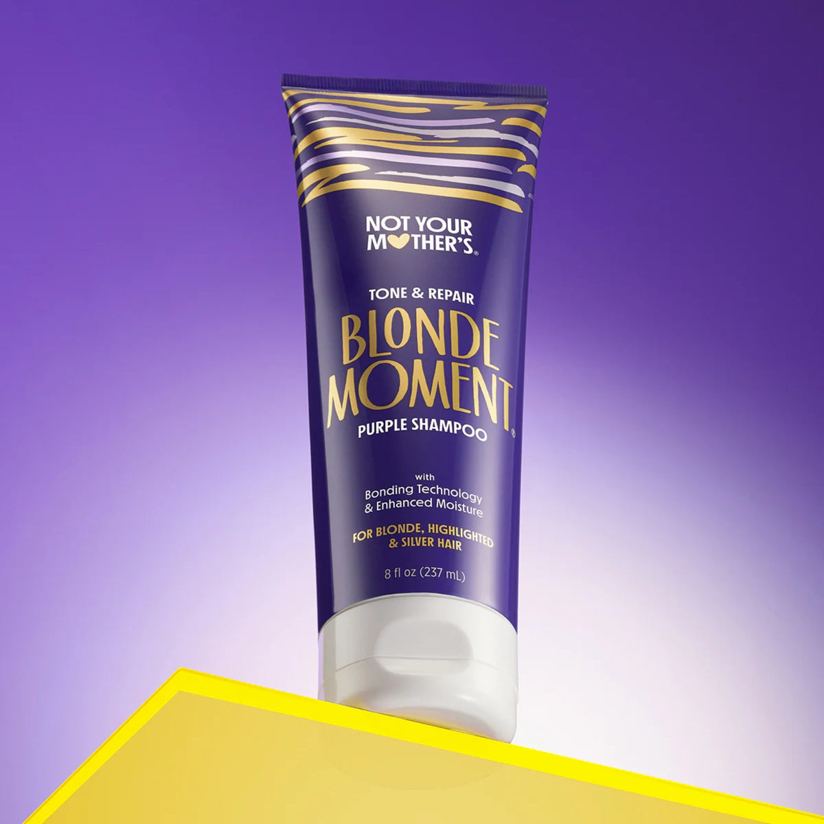 Not Your Mother's Blonde Moment purple shampoo for blonde hair in purple and gold tube on yellow table.