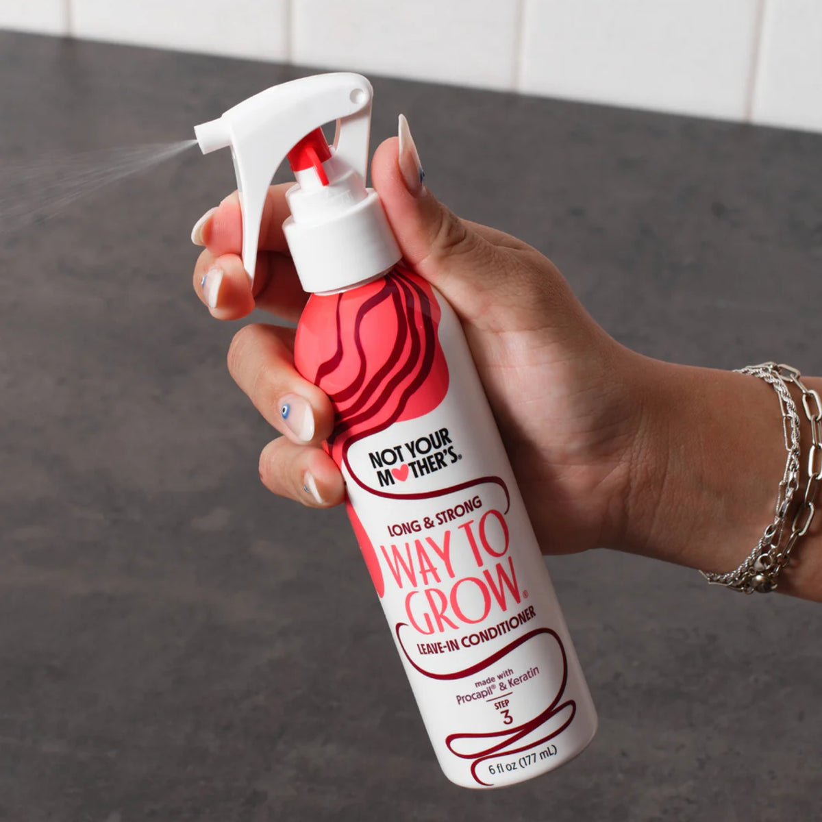Hand spray Not Your Mother's Way To Grow leave-in conditioner from white and red bottle.