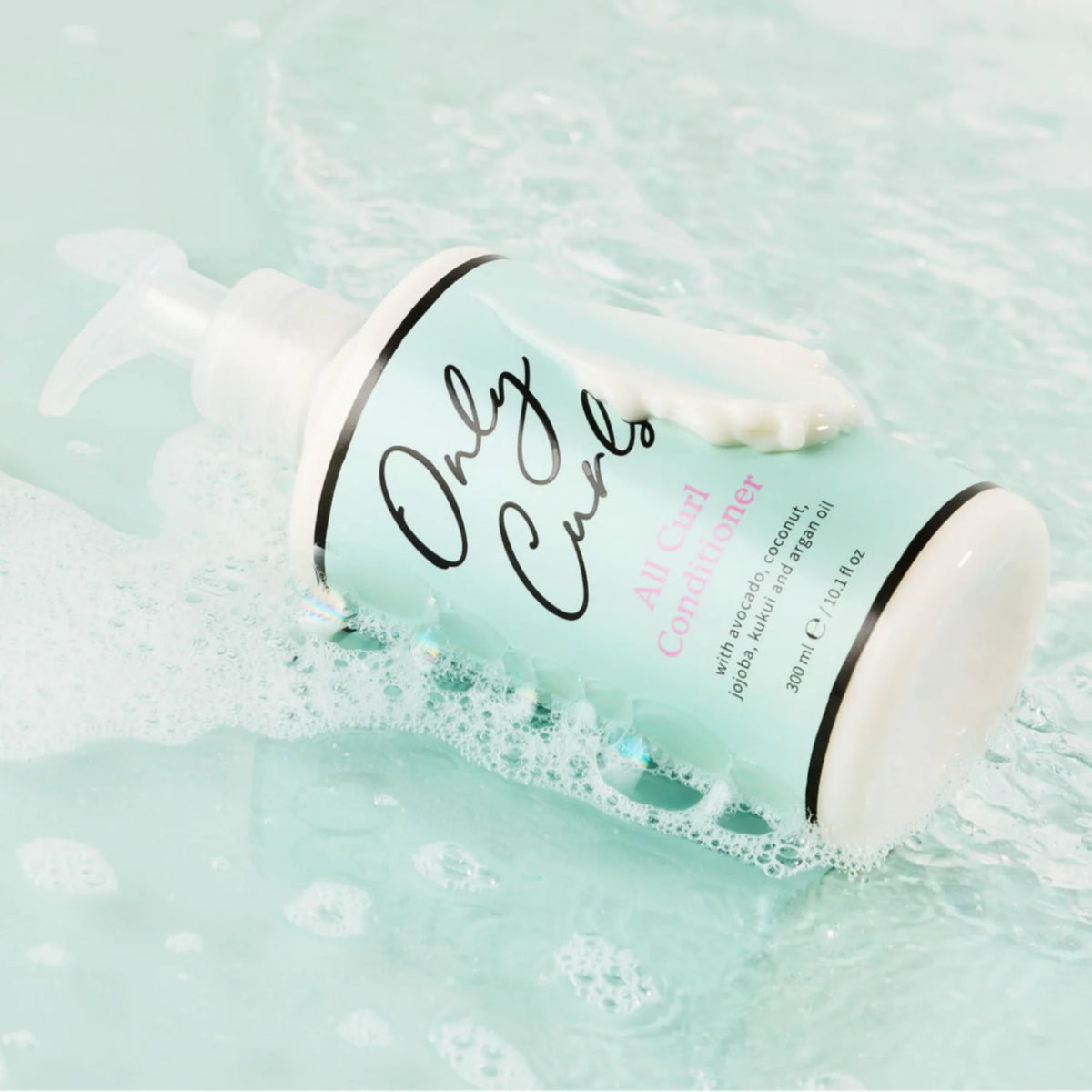 Only Curls All Curl Conditioner-flaske ligger i skummende vand med cremet hårbalsam der siver ud af pumpen.