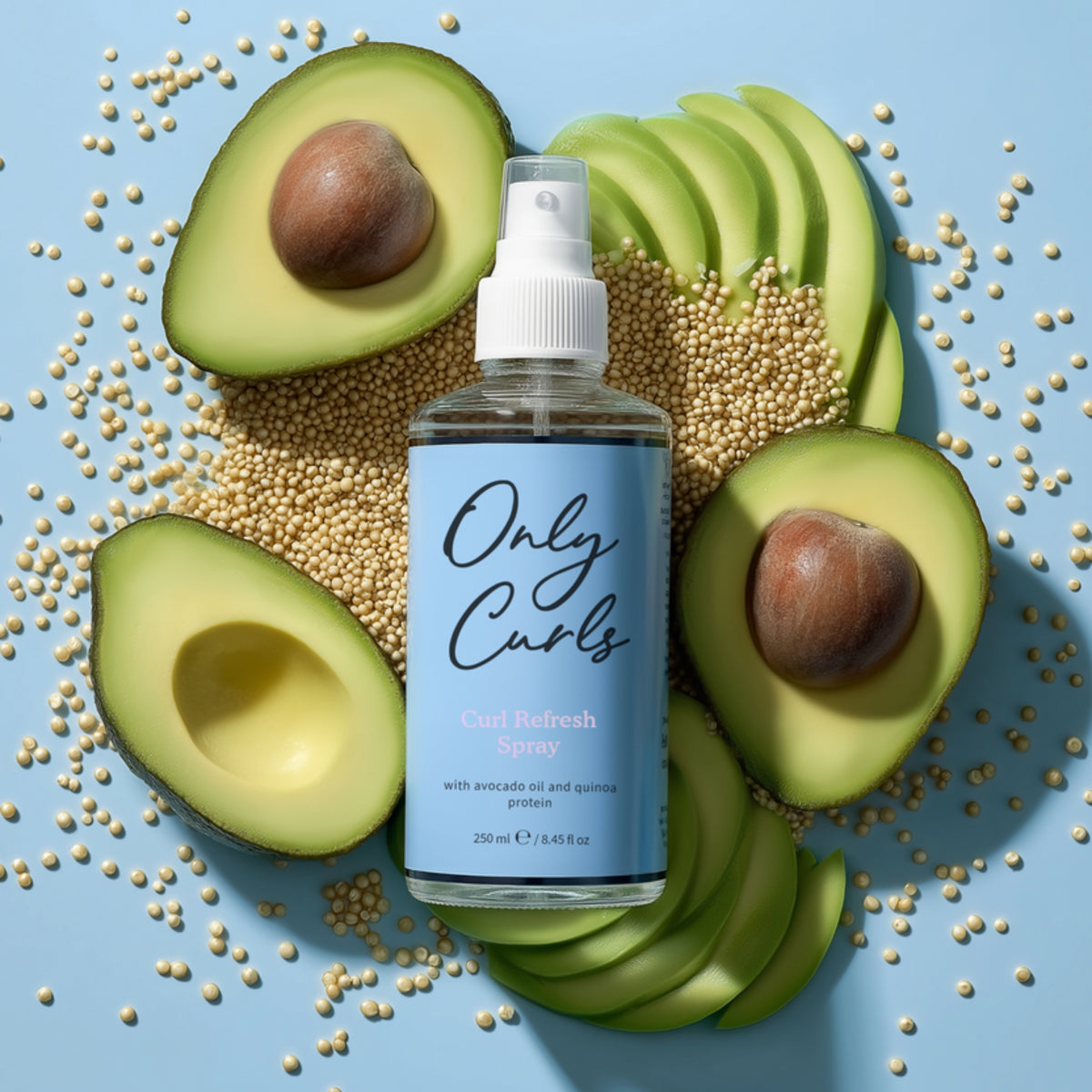 Only Curls Curl Refresh Spray-flaske omgivet af skåret avocado og quinoa på blå baggrund.