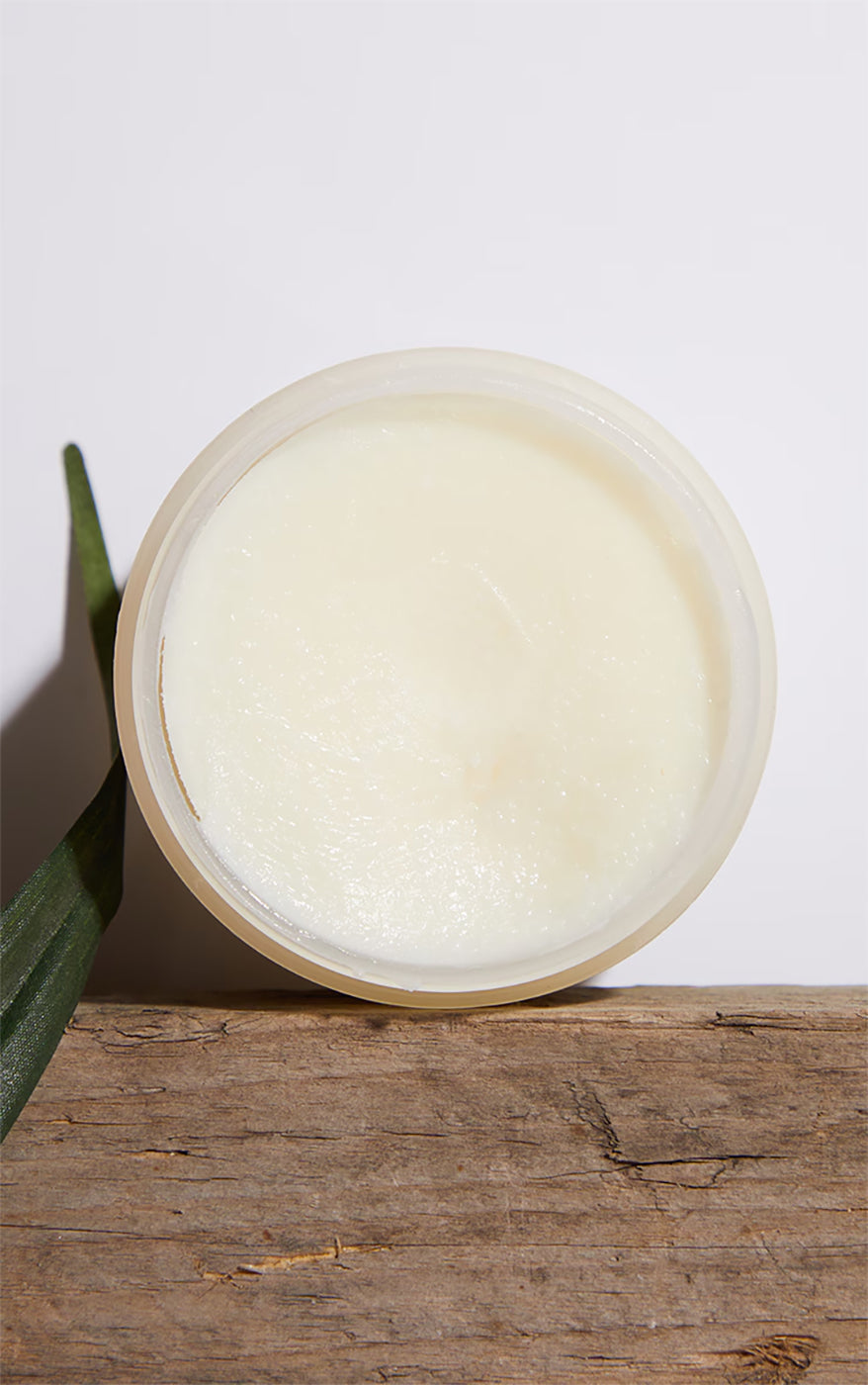 Palmers Coconut Oil Formula Body Balm in open on rustic wooden surface with green leaf.
